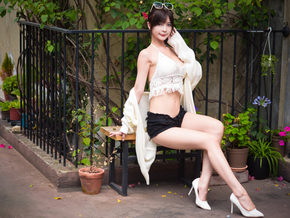 Стройная девушка азиатка сидит на лавке у дома