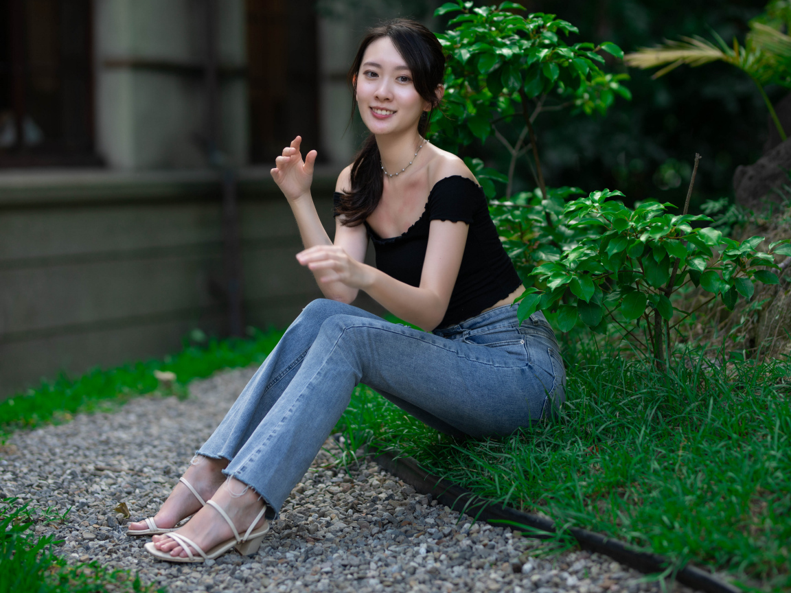 Улыбающаяся девушка азиатка сидит на зеленой траве