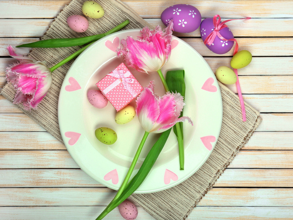 Пасхальные яйца с тюльпанами на тарелке на столе