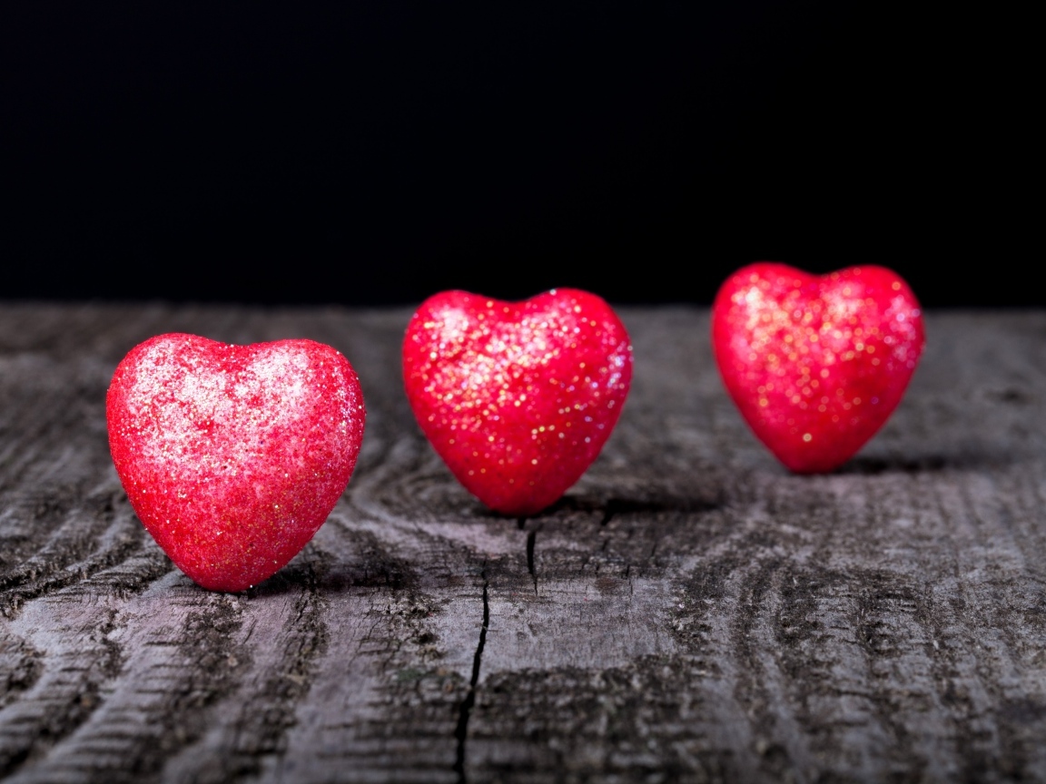 Три блестящих красных сердца на деревянном столе