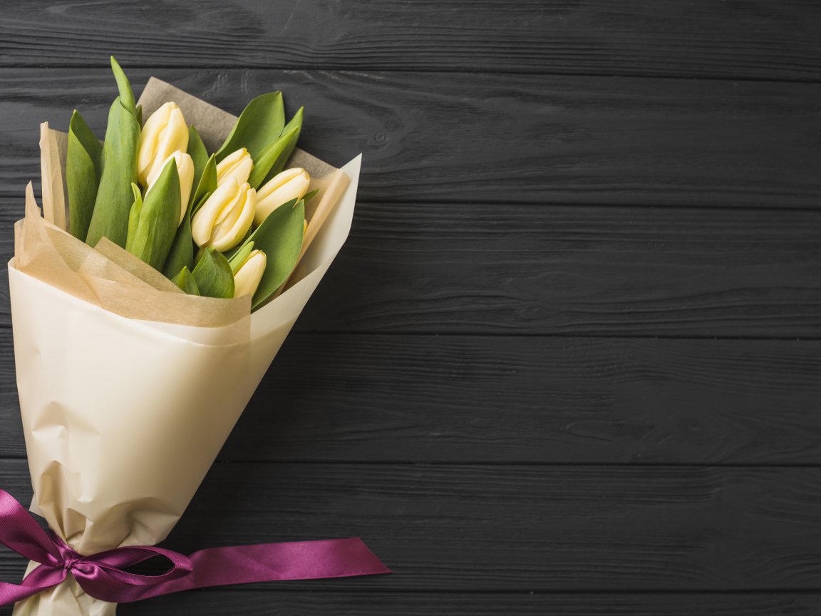 Букет желтых тюльпанов в бумаге на черном столе