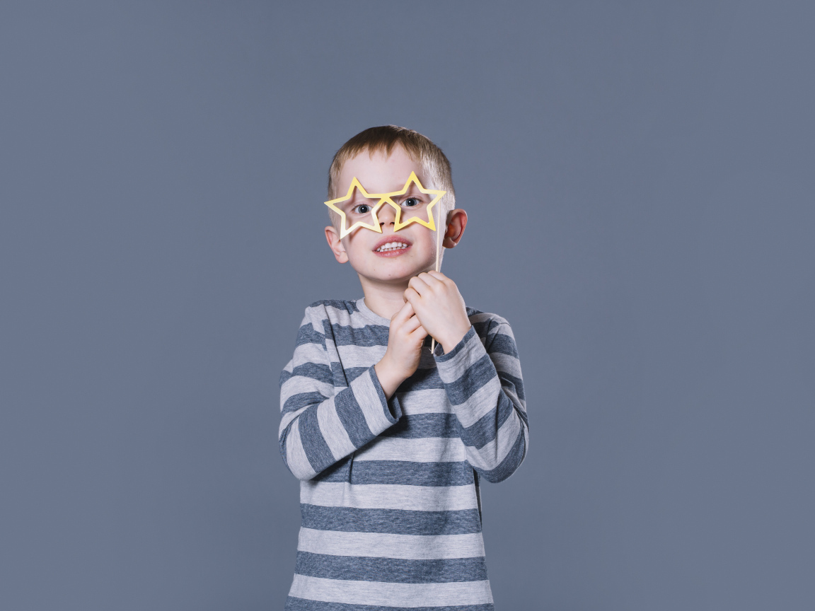 Маленький мальчик с очками в форме звезд на сером фоне