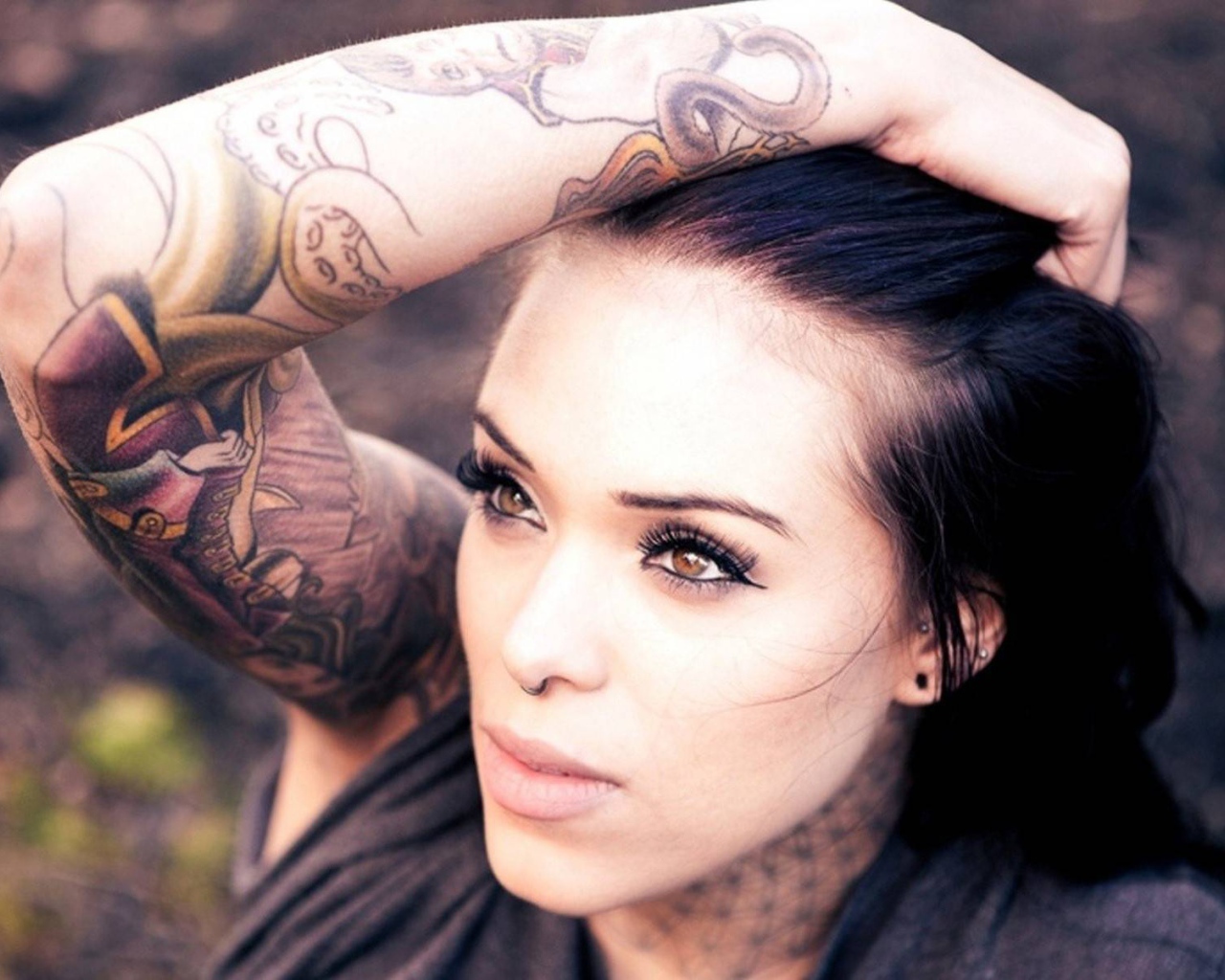 Девушка брюнетка с пирсингом в носу и татуировкой на руке