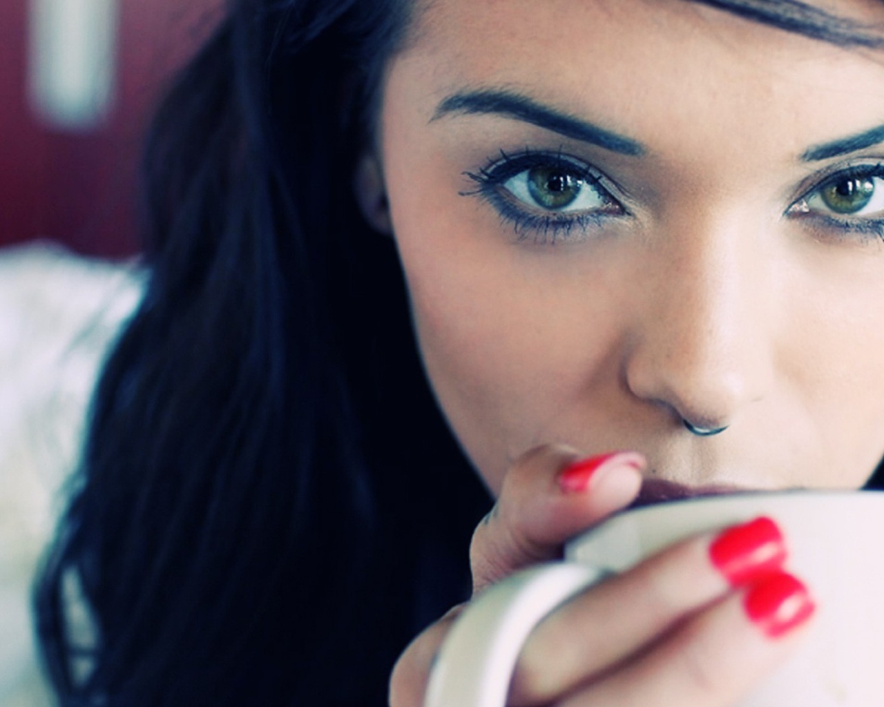 Девушка брюнетка с пирсингом в носу и красными ногтями