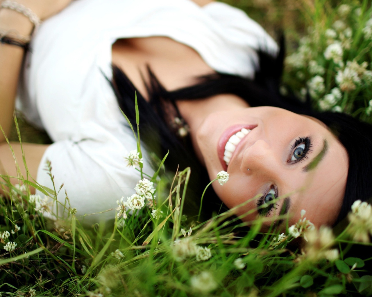 Девушка брюнетка с пирсингом в носу лежит в траве