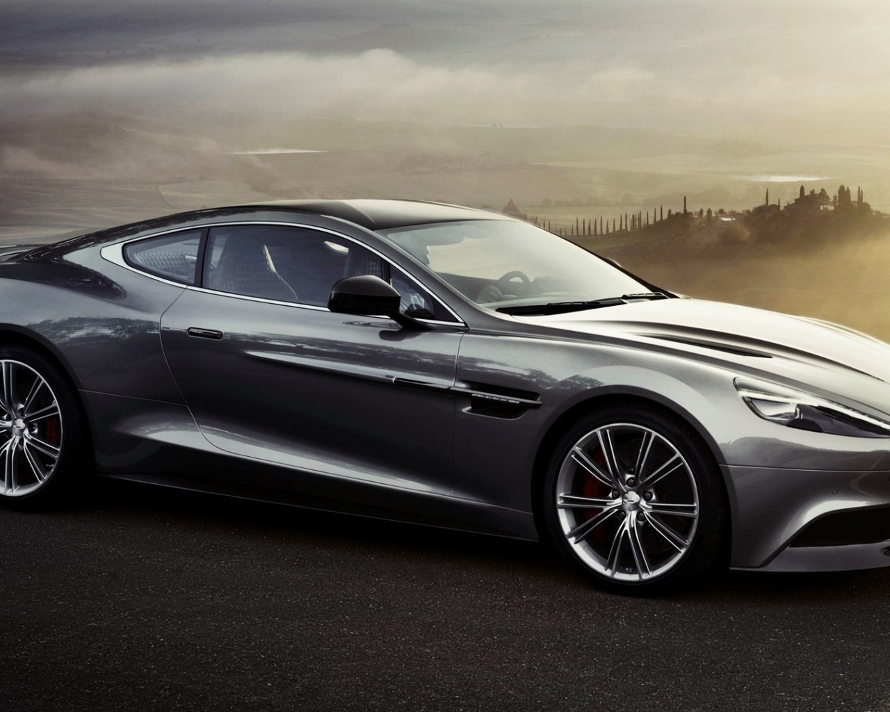 Темно серый Aston Martin на фоне туманной долины