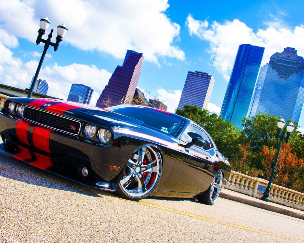 Черный Dodge Challenger с красными полосами на фоне небоскребов