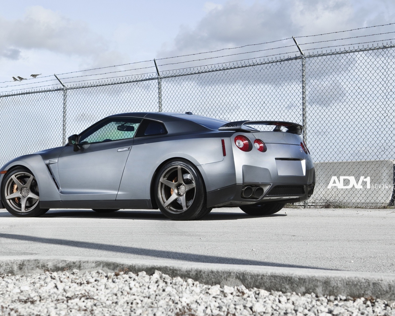 Серый Nissan Skyline GT-R R35 у забора из сетки