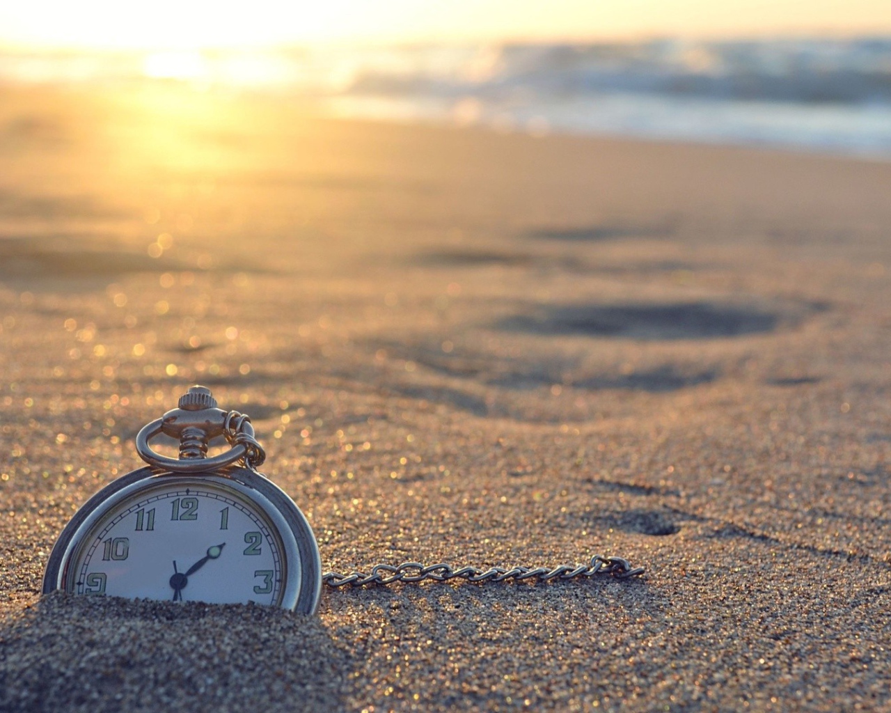 Часы на цепочке лежат в песке