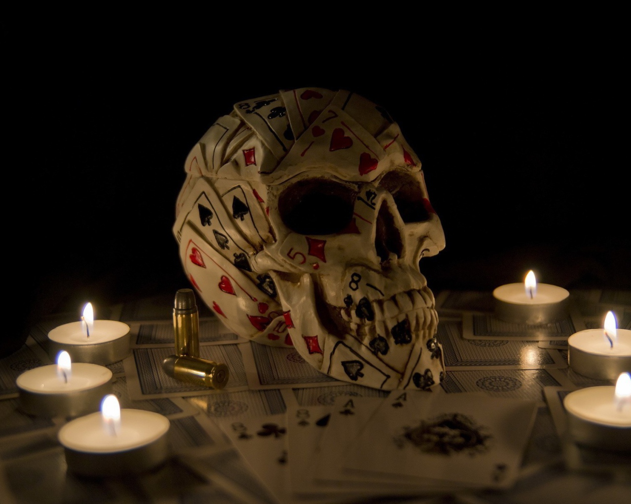 Череп из игровых карт среди свечей