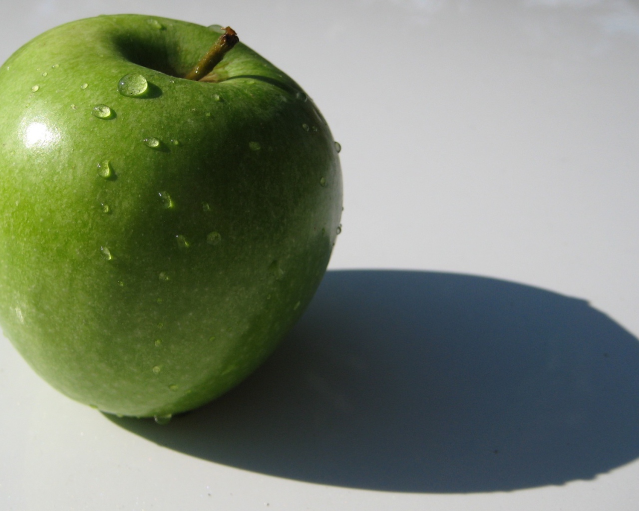 Зеленое яблоко на белой поверхности