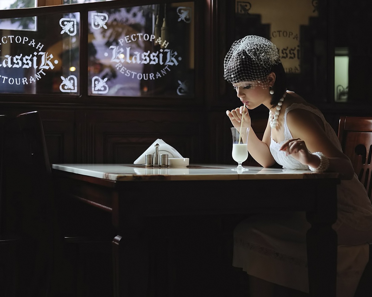 Девушка в белом платье пьет коктейль в ресторане
