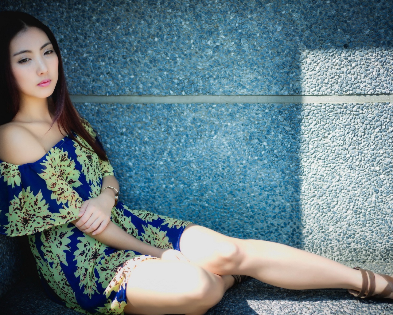 Девушка сидит в тени у гранитной стены