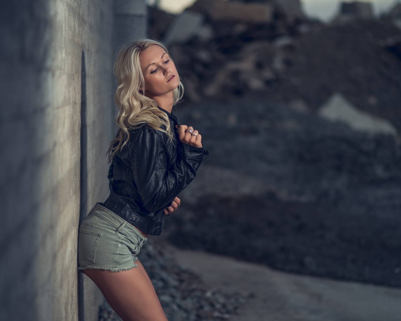 Блондинка в джинсовых шортах стоит у стены