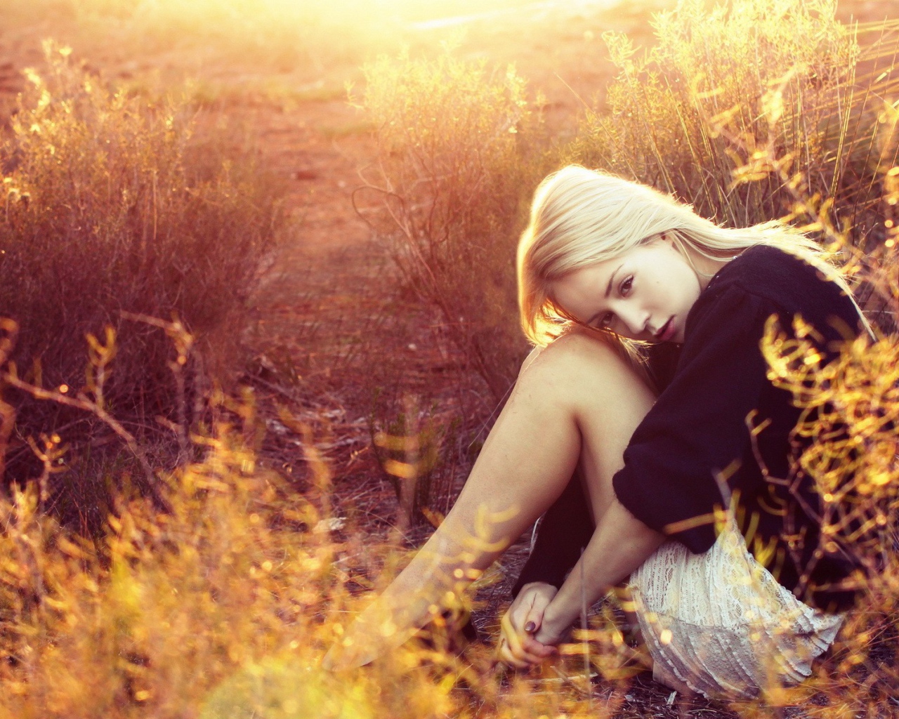 Блондинка сидит среди кустарников