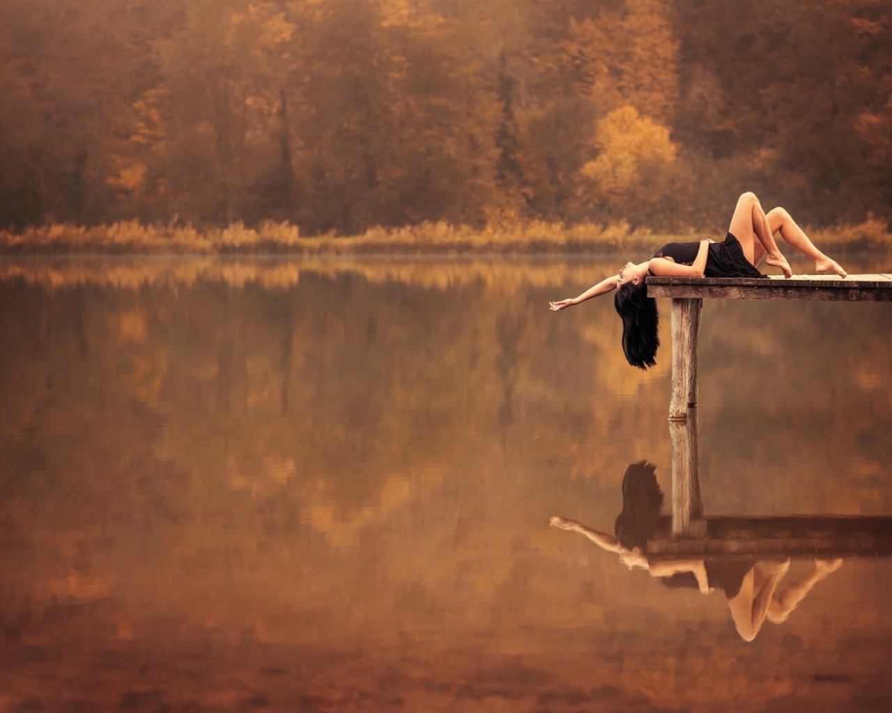 Брюнетка лежит на пирсе на озере