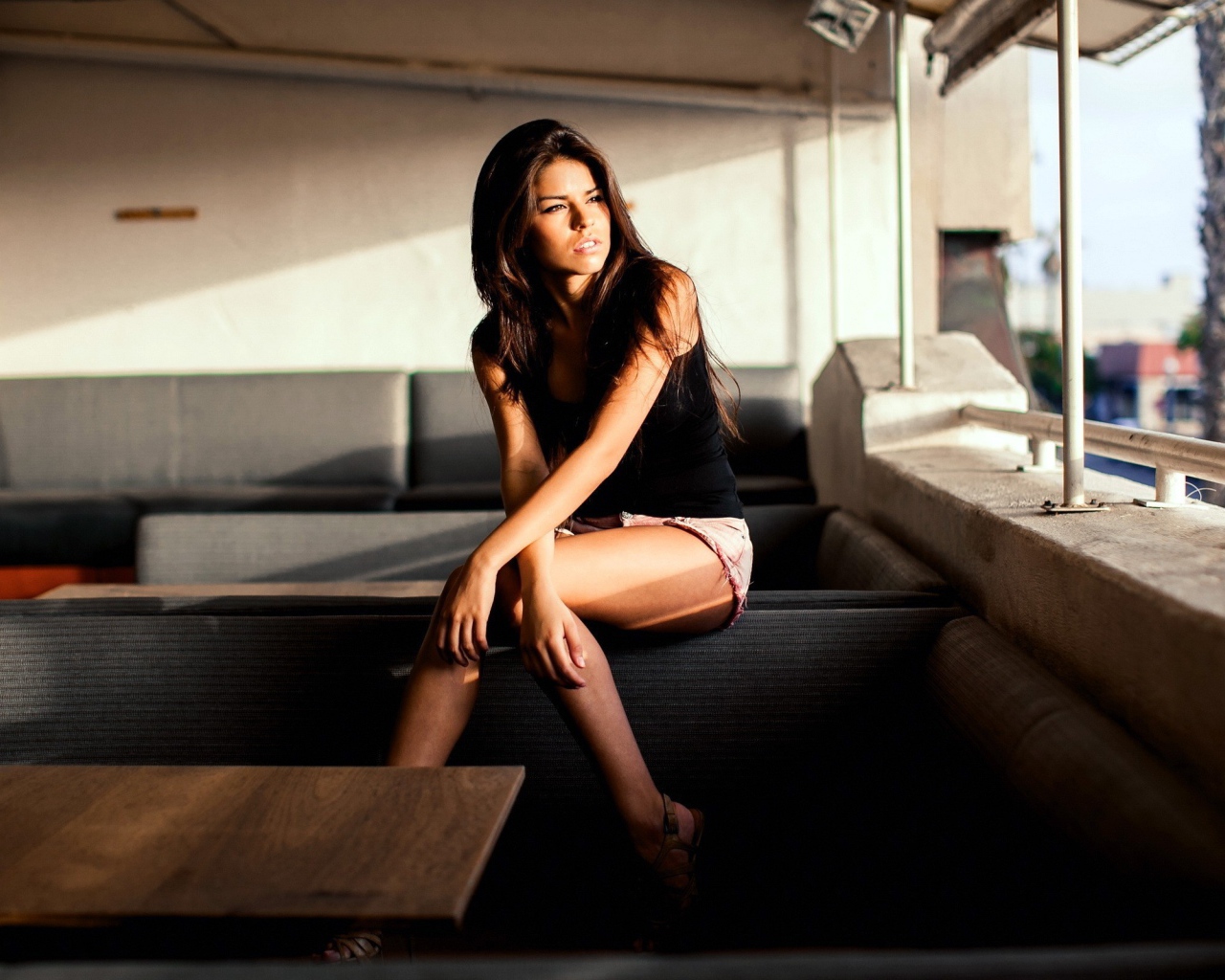 Брюнетка сидит на спинке дивана и смотрит в окно