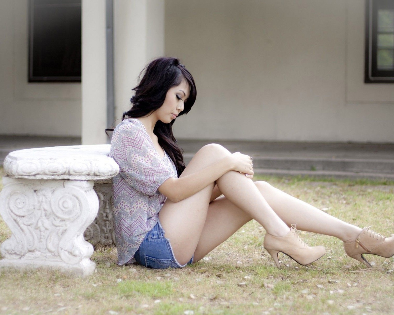Brunette sitting on the ground near a stone bench