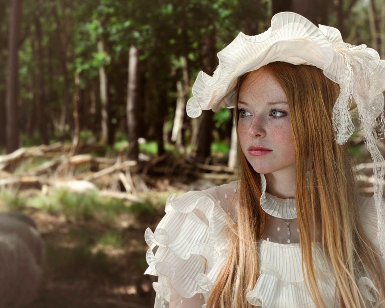 Веснушчатая девушка в белой шляпке стоит у дерева