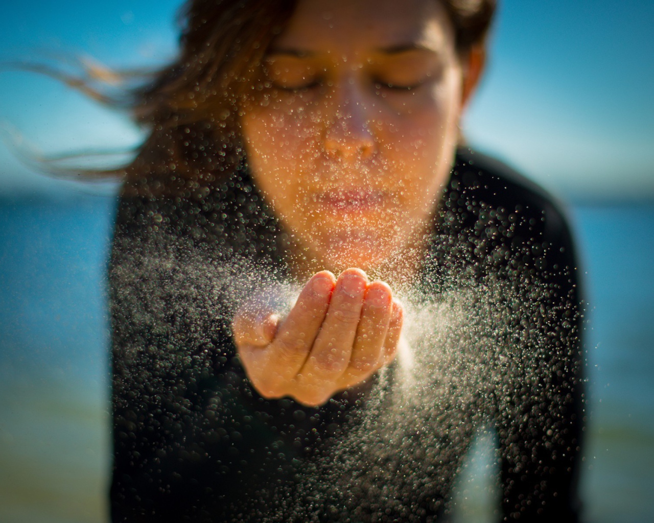 Девушка сдувает песок с руки