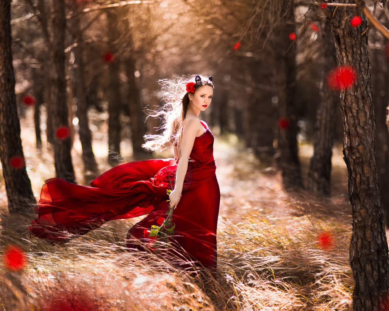 Девушка в красном платье стоит в ветренном лесу