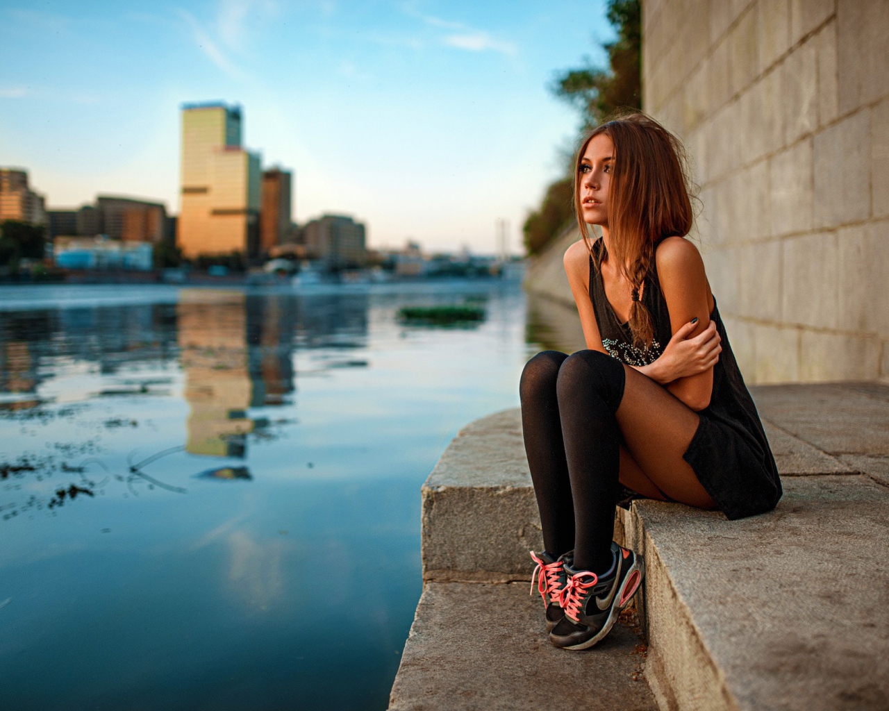 Девушка в кедах сидит на набережной