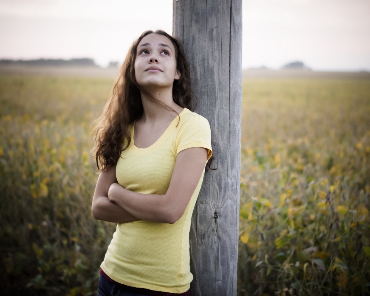 Девушка в желтой майке стоит у столба