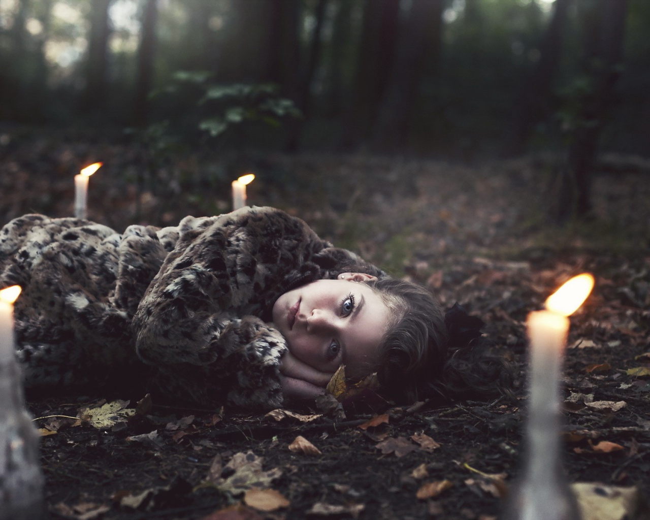 Девушка лежит среди свечей в лесу