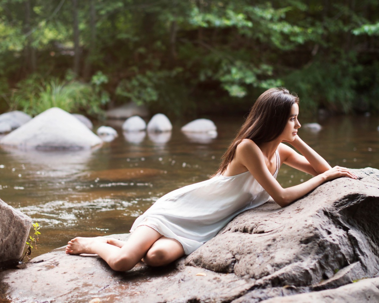 Девушка лежит на камне у реки