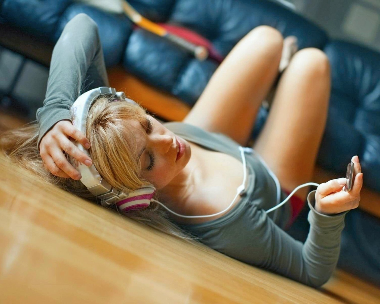 Девушка лежит на паркете и слушает музыку в наушниках