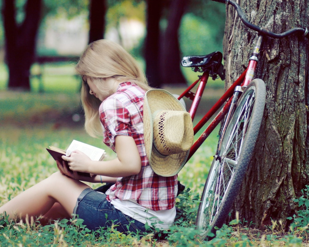 Девушка читает книгу сидя в парке на газоне