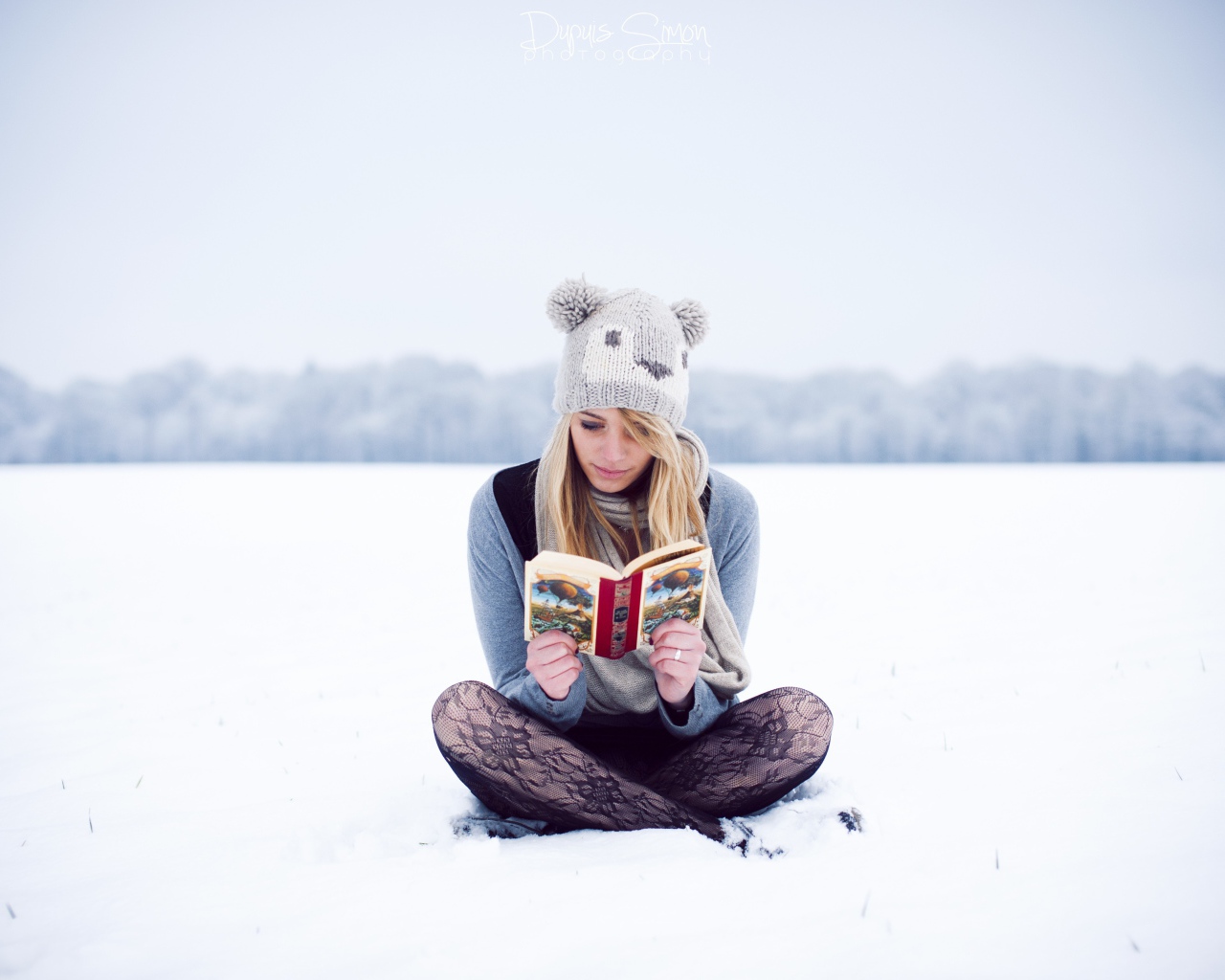 Девушка читает книгу сидя на снегу