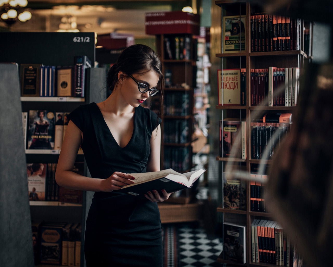 Девушка читает среди книжных полок