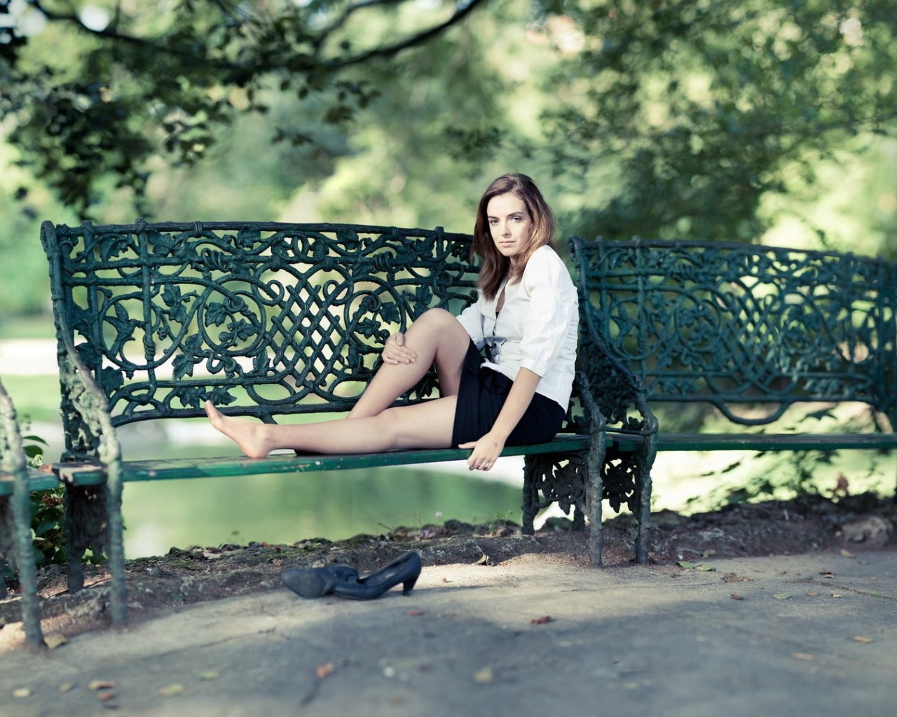 Девушка сидит на кованной парковой скамье