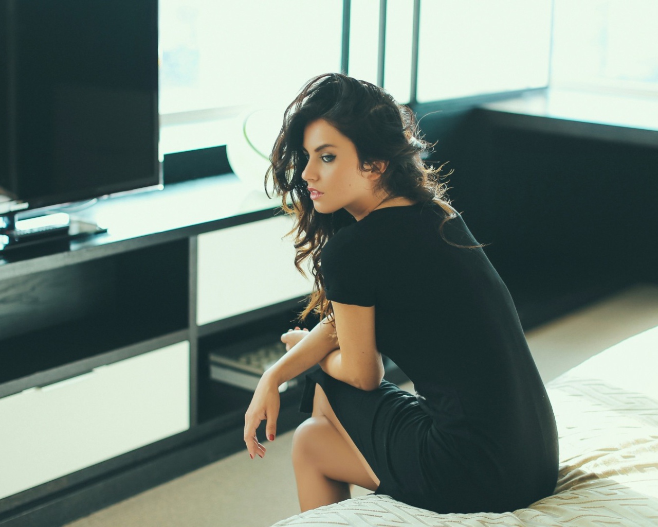 Девушка сидит на кровати перед телевизором