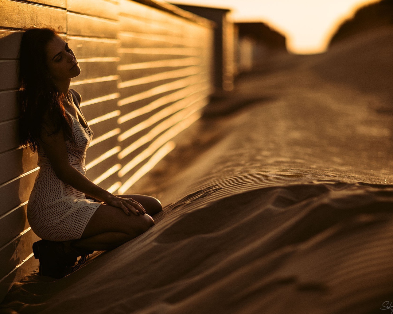 Девушка сидит на песке у забора
