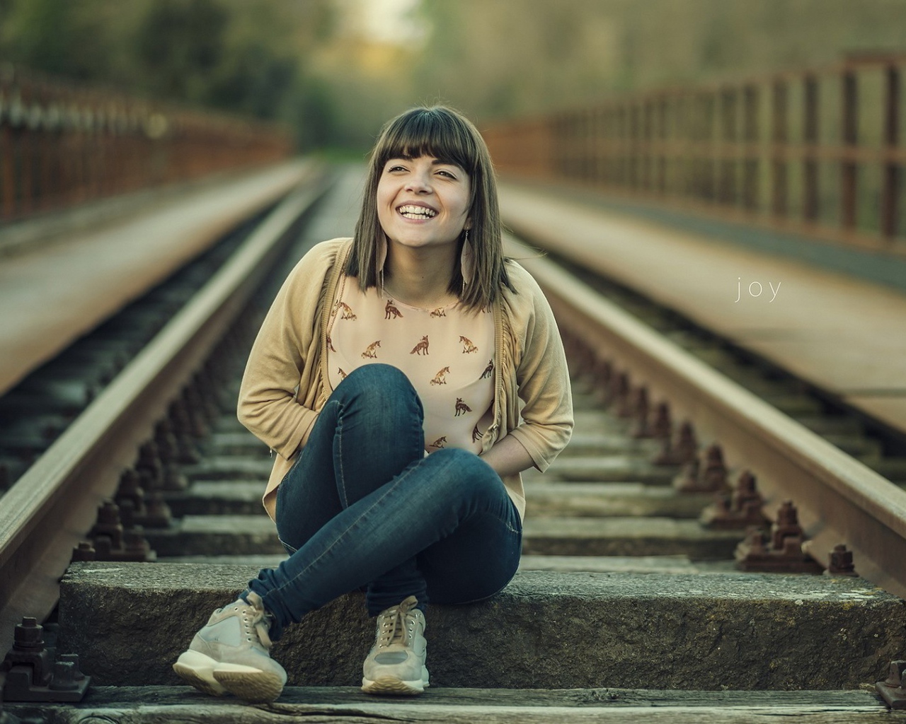 Девушка улыбается сидя на рельсах