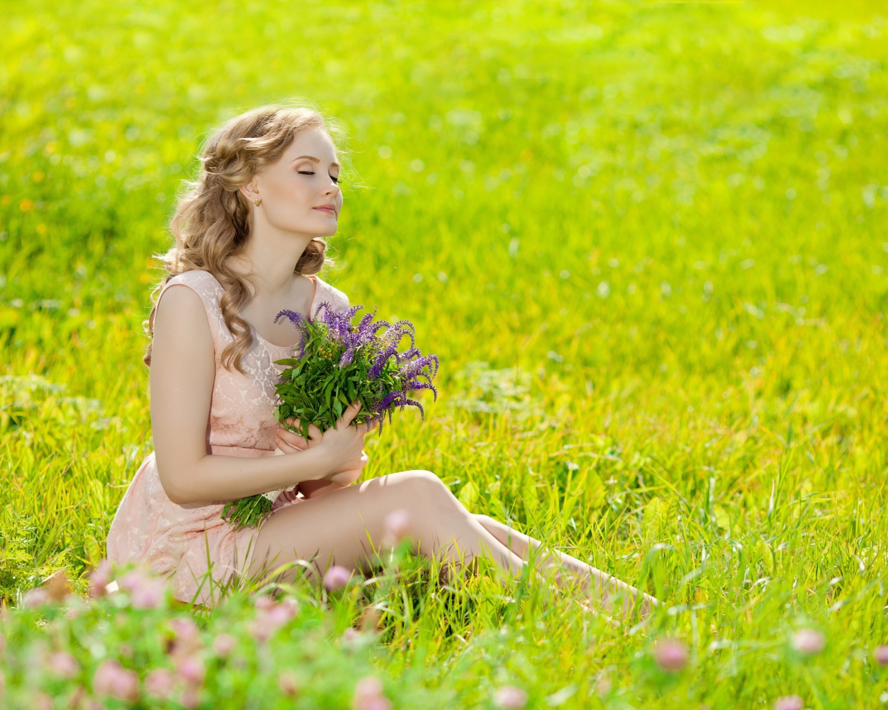 Девушка с букетом сидит на зеленой траве