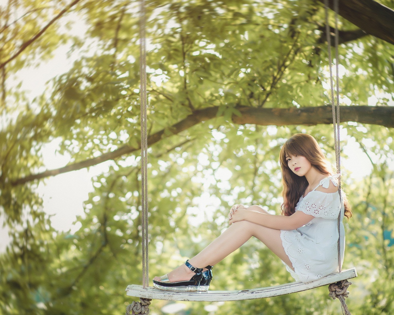 Японская девушка в белом платье сидит на качелях