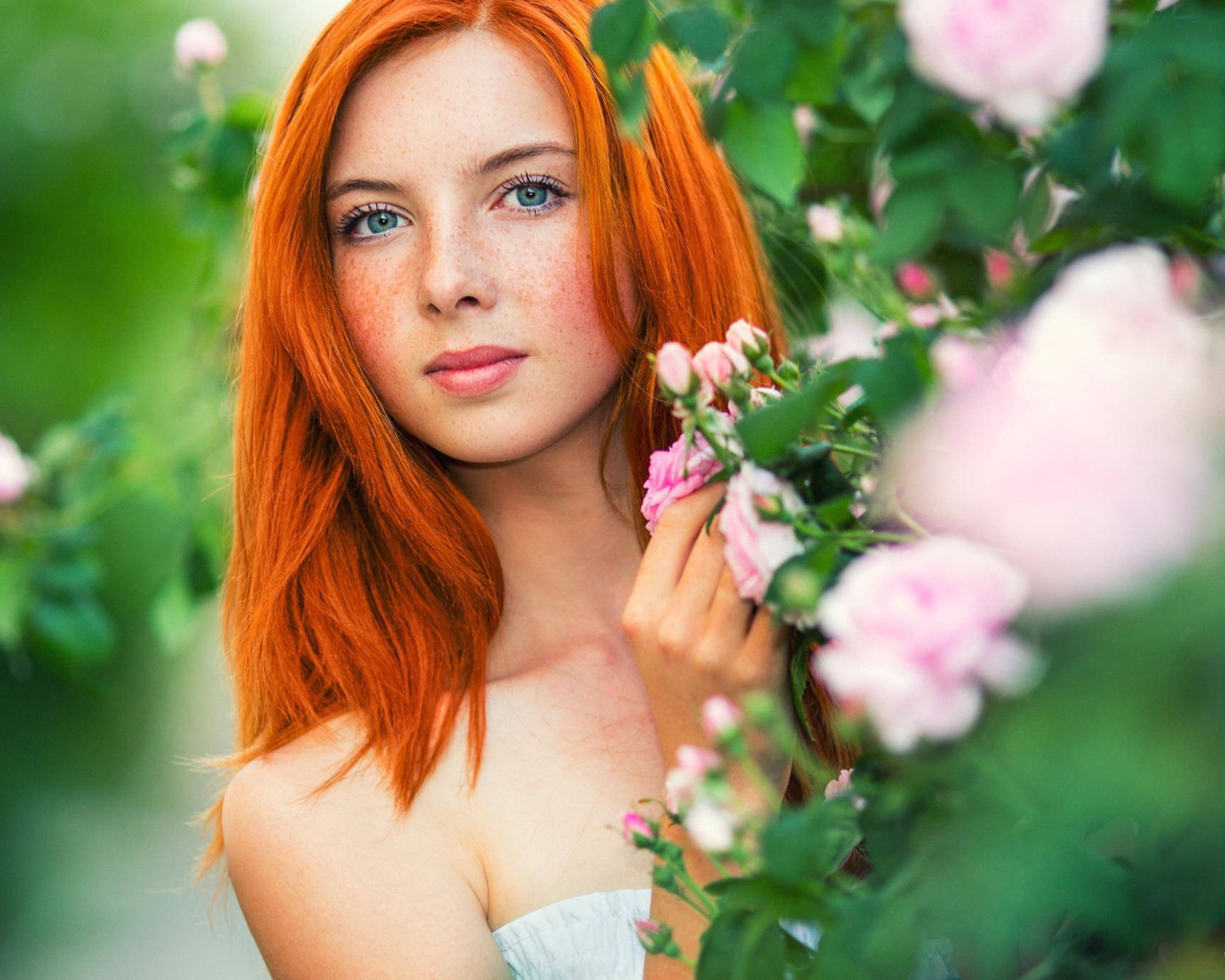 Рыжая девушка прячется за цветущими ветками