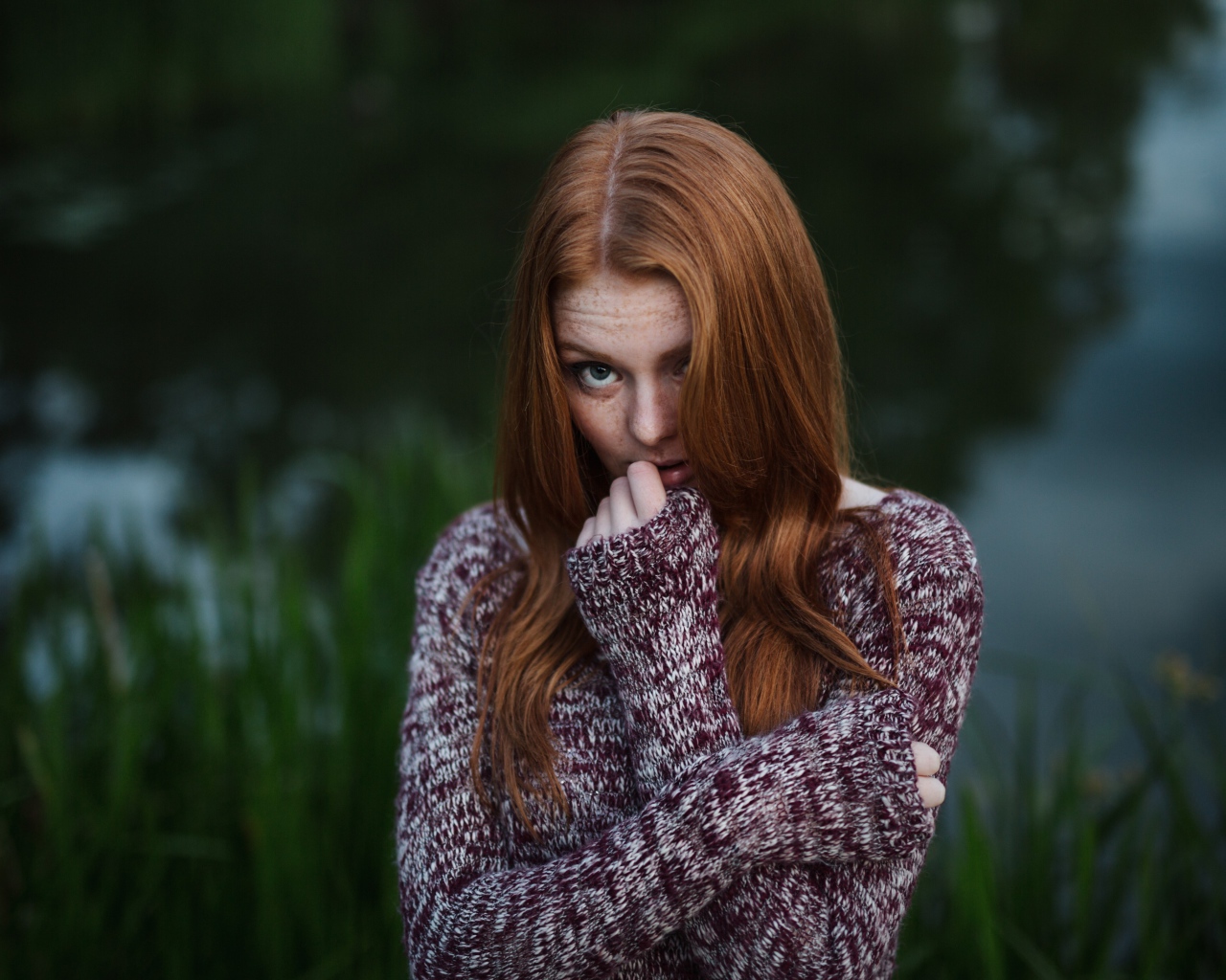 Рыжая девушка в свитере на фоне водоема