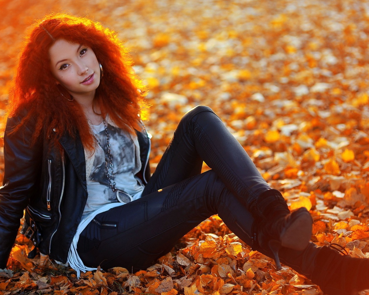 Рыжая девушка сидит на ковре из желтых листьев
