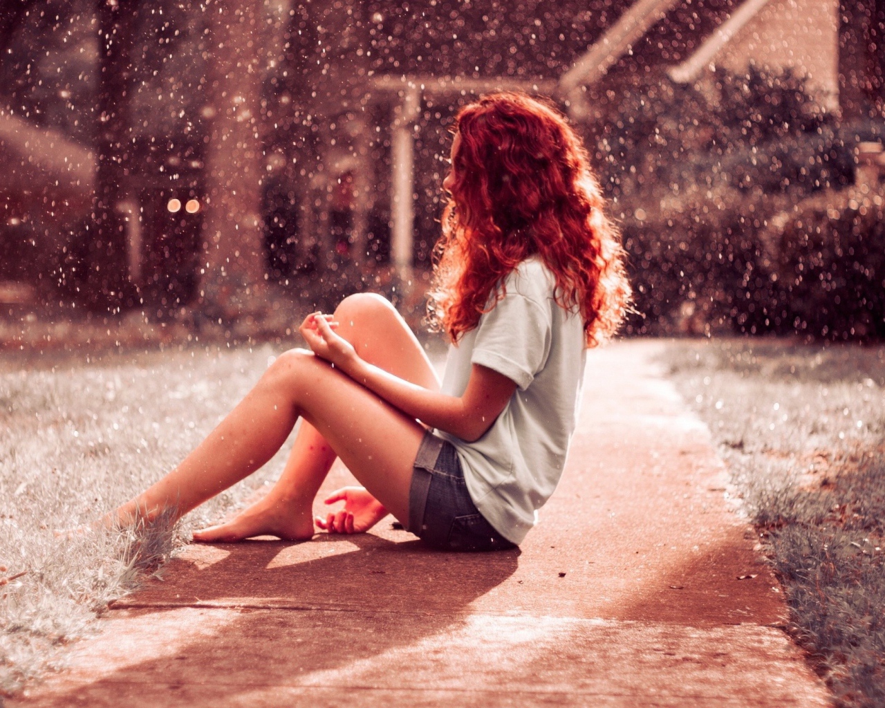Рыжая девушка сидит на земле во время дождя