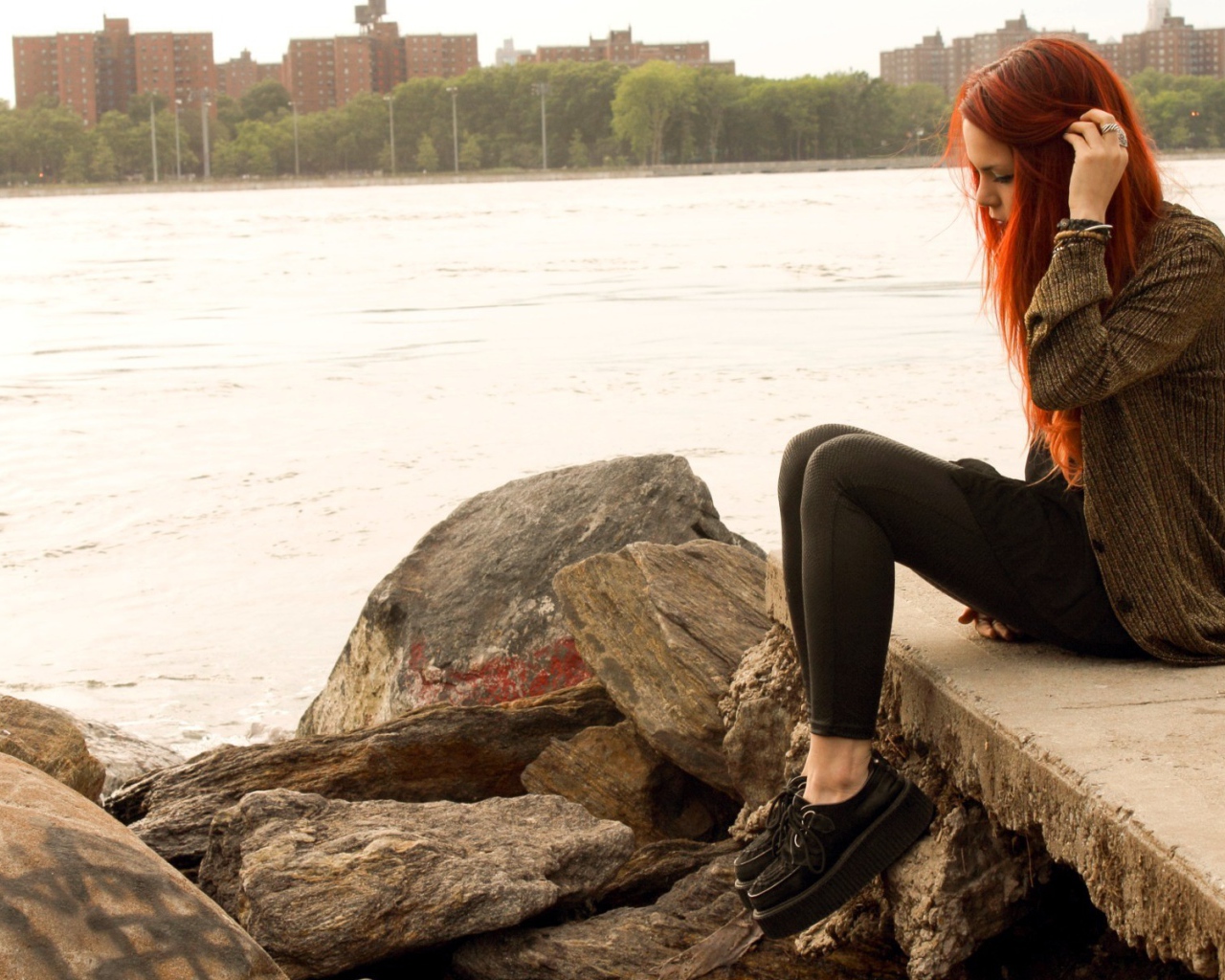 Рыжая девушка сидит на плитах набережной