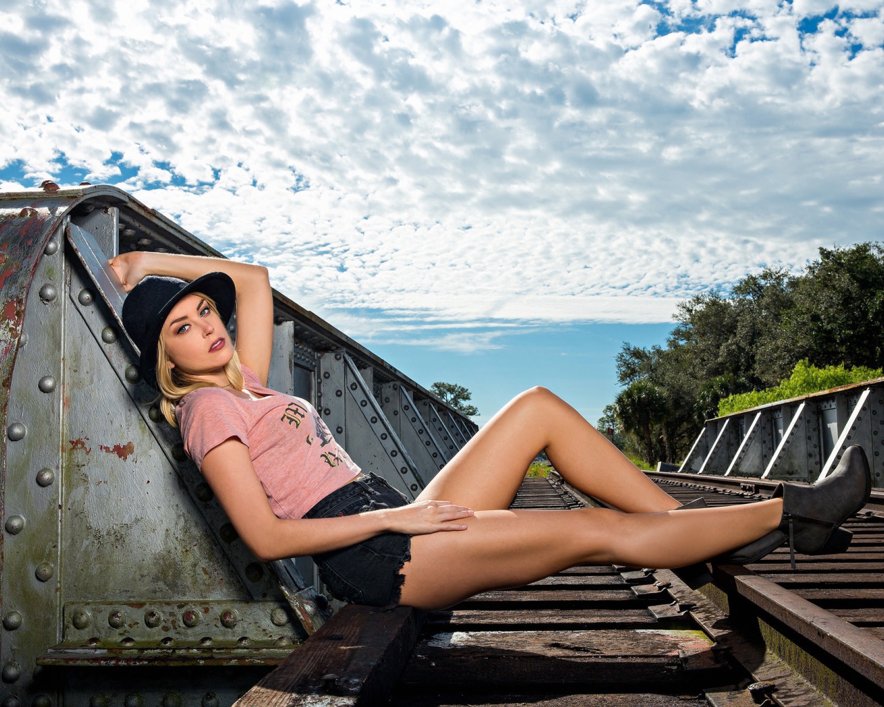 Блондинка в шляпе позирует на железной дороге