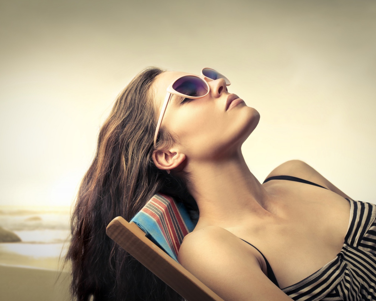 Девушка в очках загорает в шезлонге