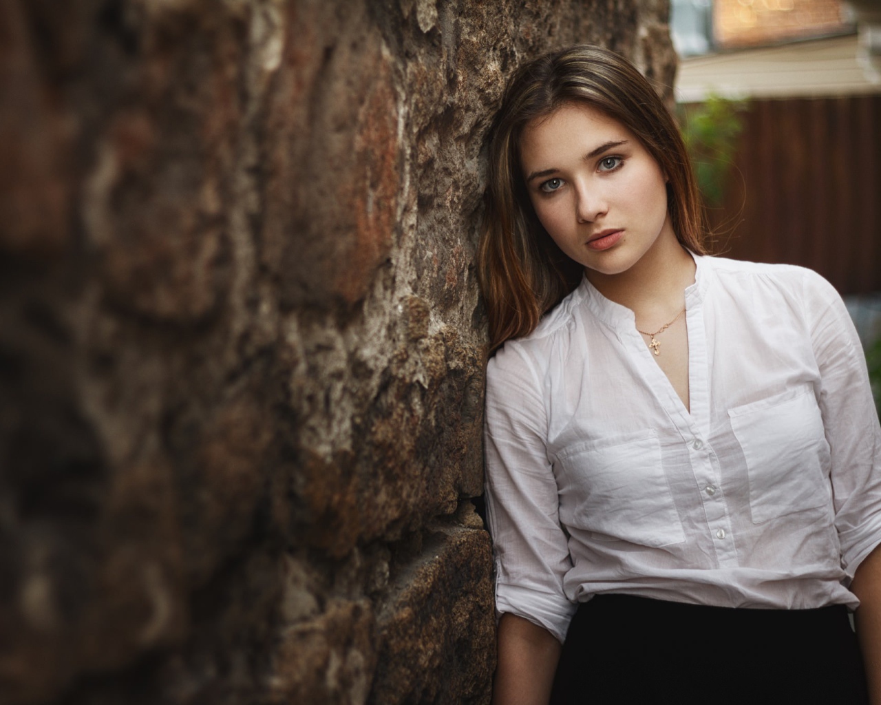 Девушка в белой рубашке стоит у стены