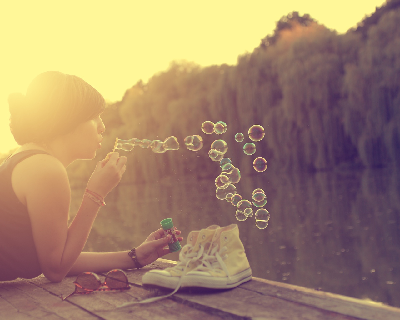 Девушка лежит на пирсе и играет с мыльными пузырями