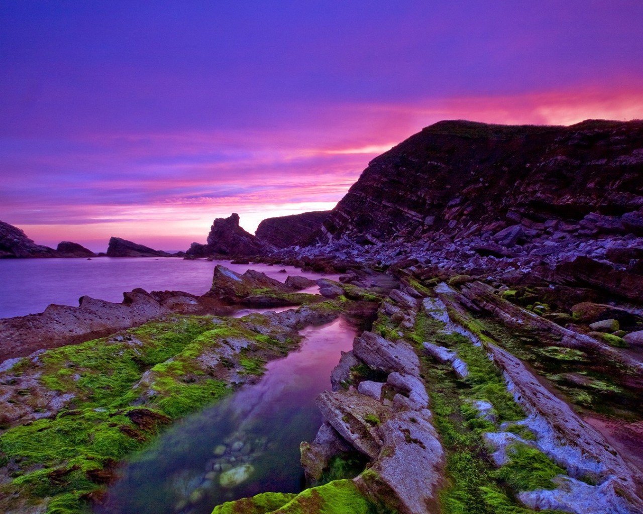 Голые скалы у берега на фоне сиреневого заката