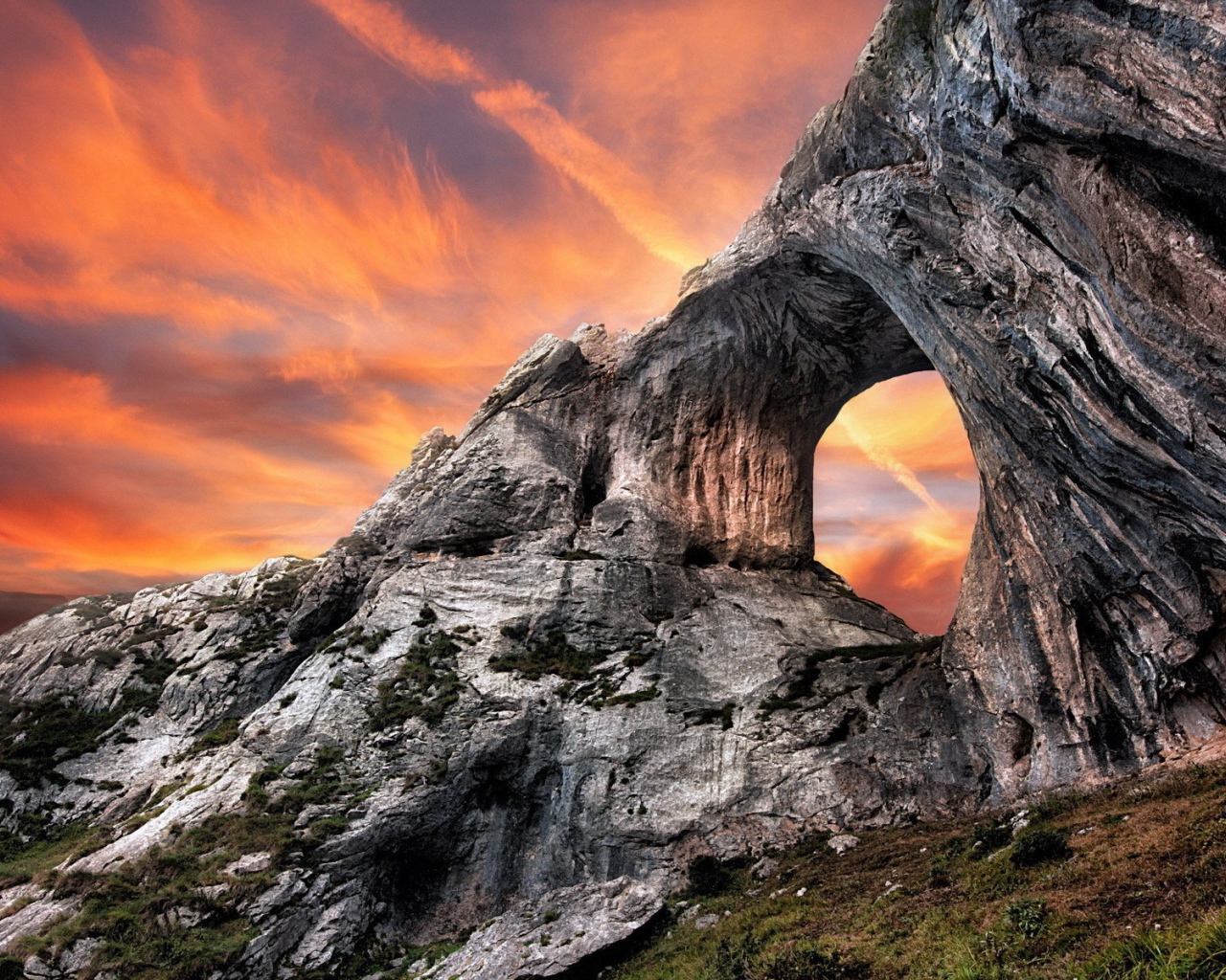 Овальный проход в скале на фоне оранжевого неба